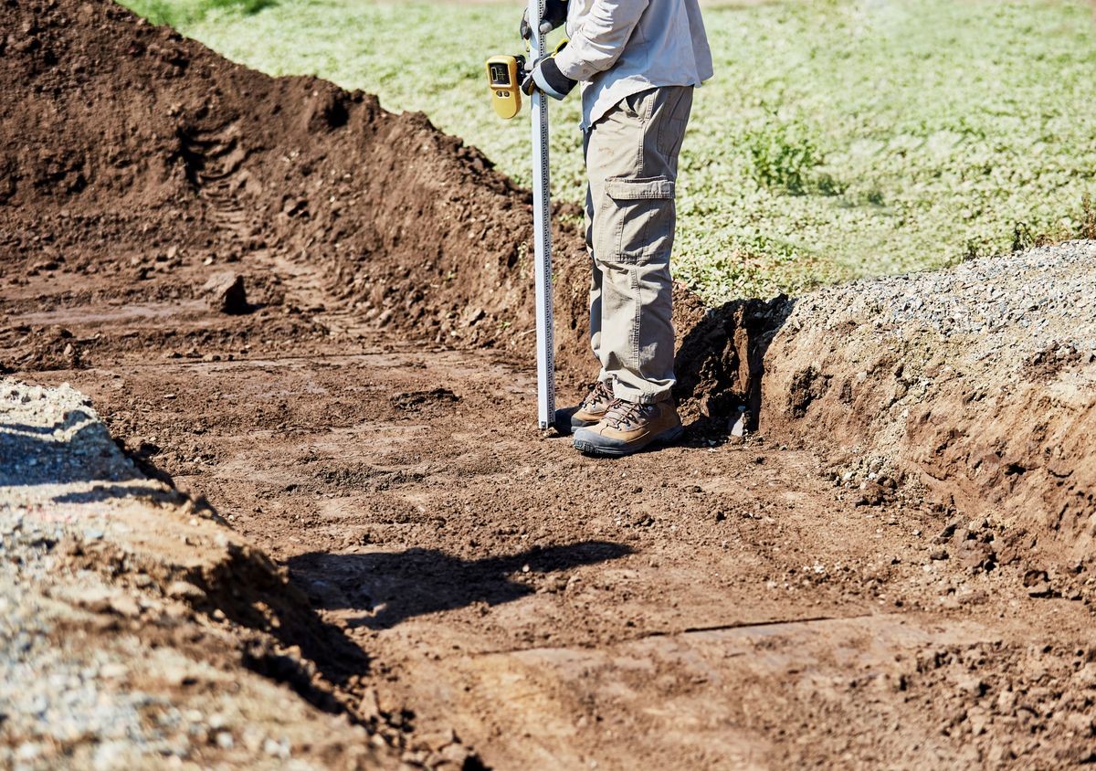 Man measuring the depth of a  trench dug for a culvert on a driveway